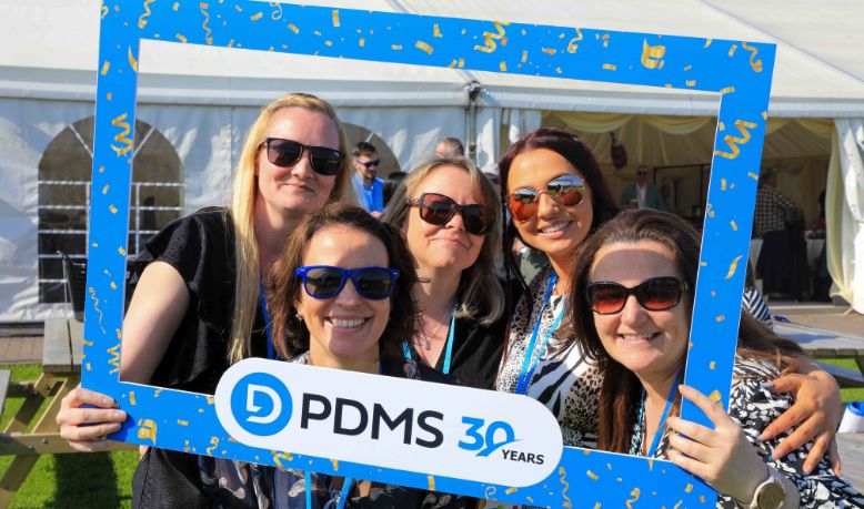  A photo of five women smiling with a PDMS 30 Years frame