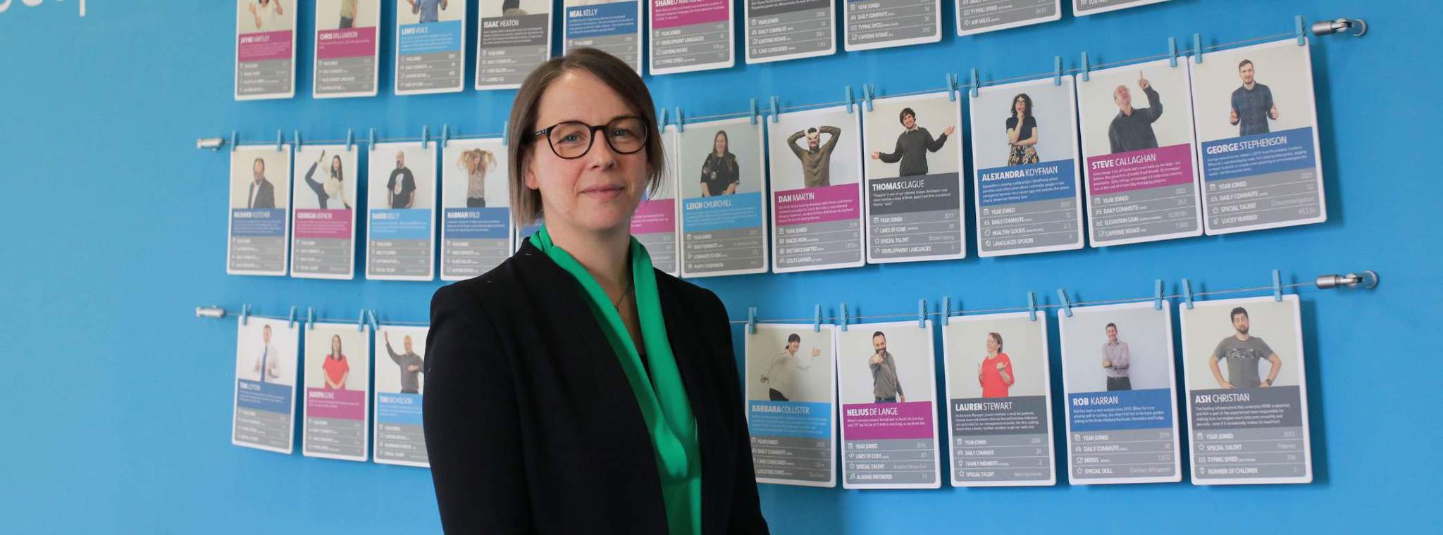 A photo of Catriona Watt, Chief Commercial Officer posing with 'our people' wall