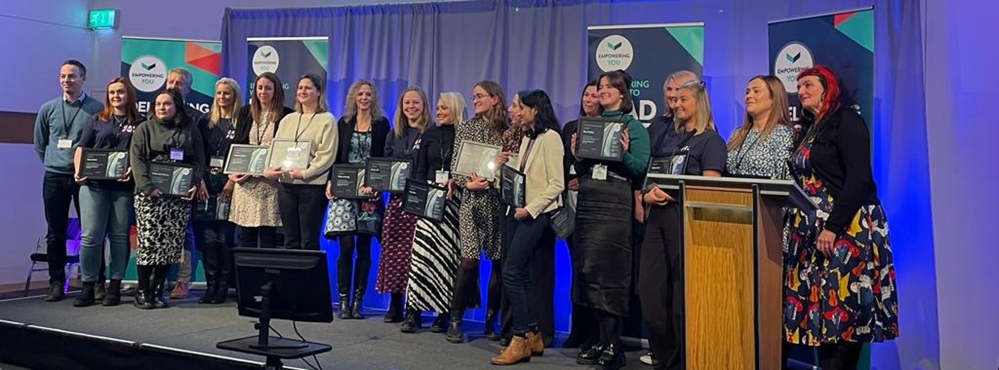 Women standing on stage holding certificates at their graduation