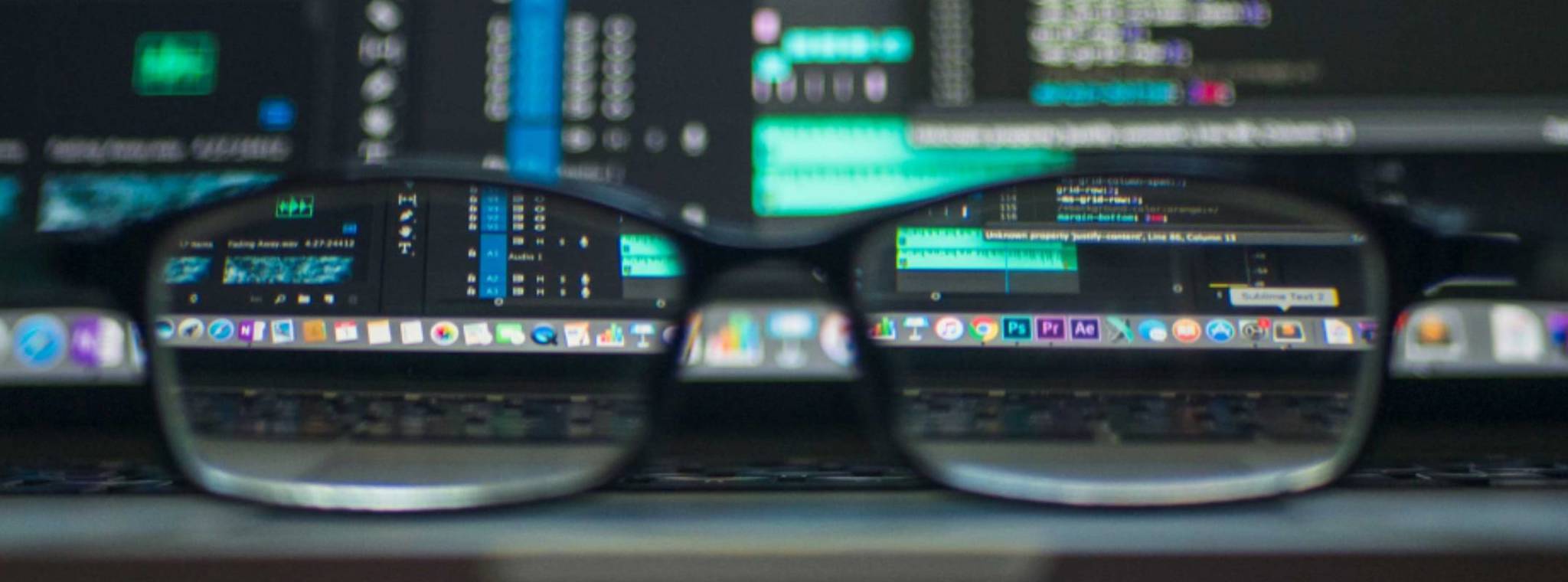 A pair of glasses resting on the front of a laptop with code on the screen