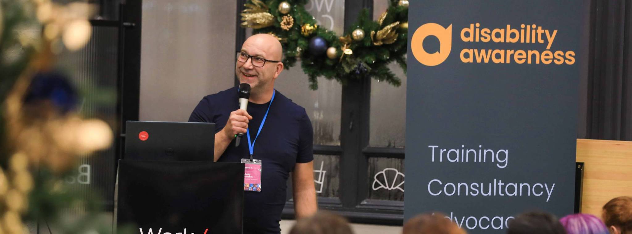 An image of Andy Hodkin speaking at a podium with a microphone