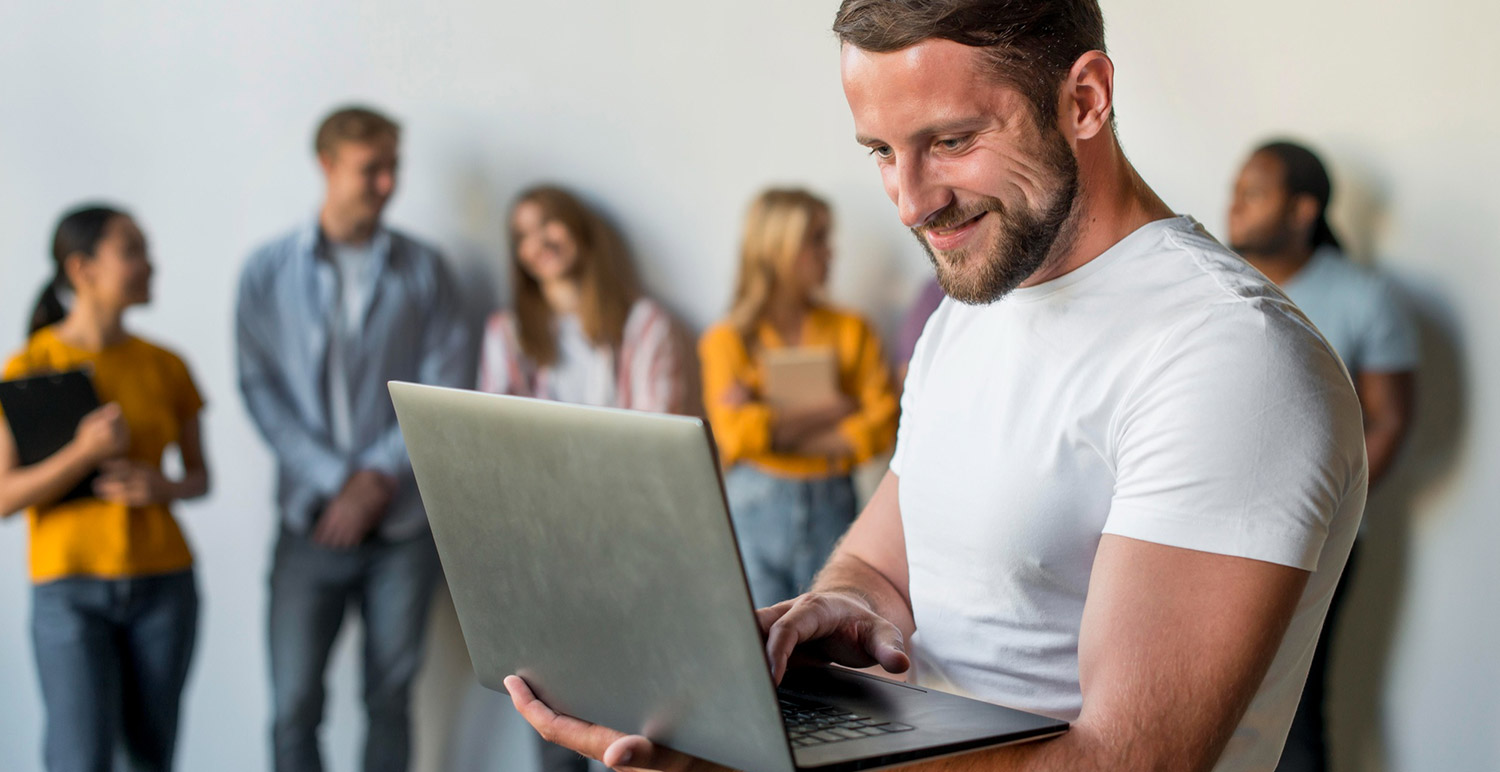 Man browsing on a laptop with people behind him