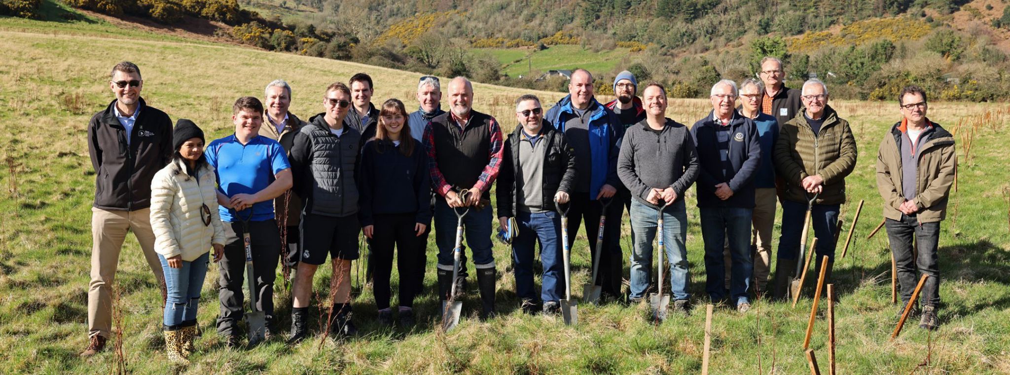 A large group of people posing with shovels with the Manx hillside in the background