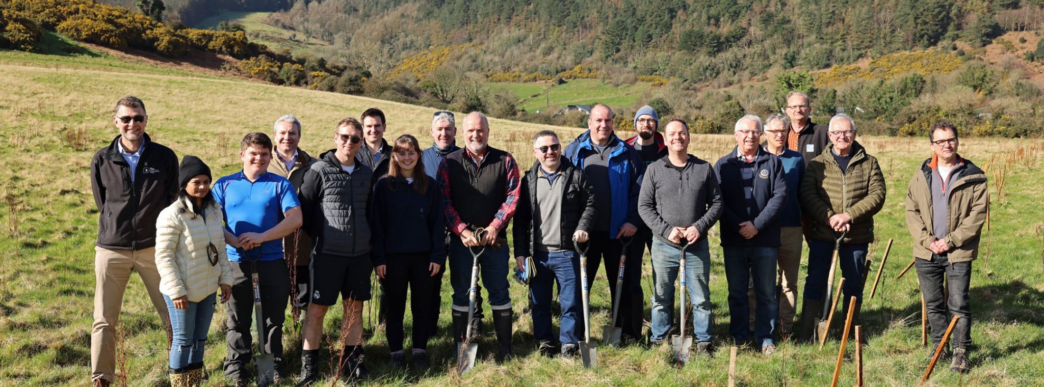 A large group of people posing with shovels with the Manx hillside in the background