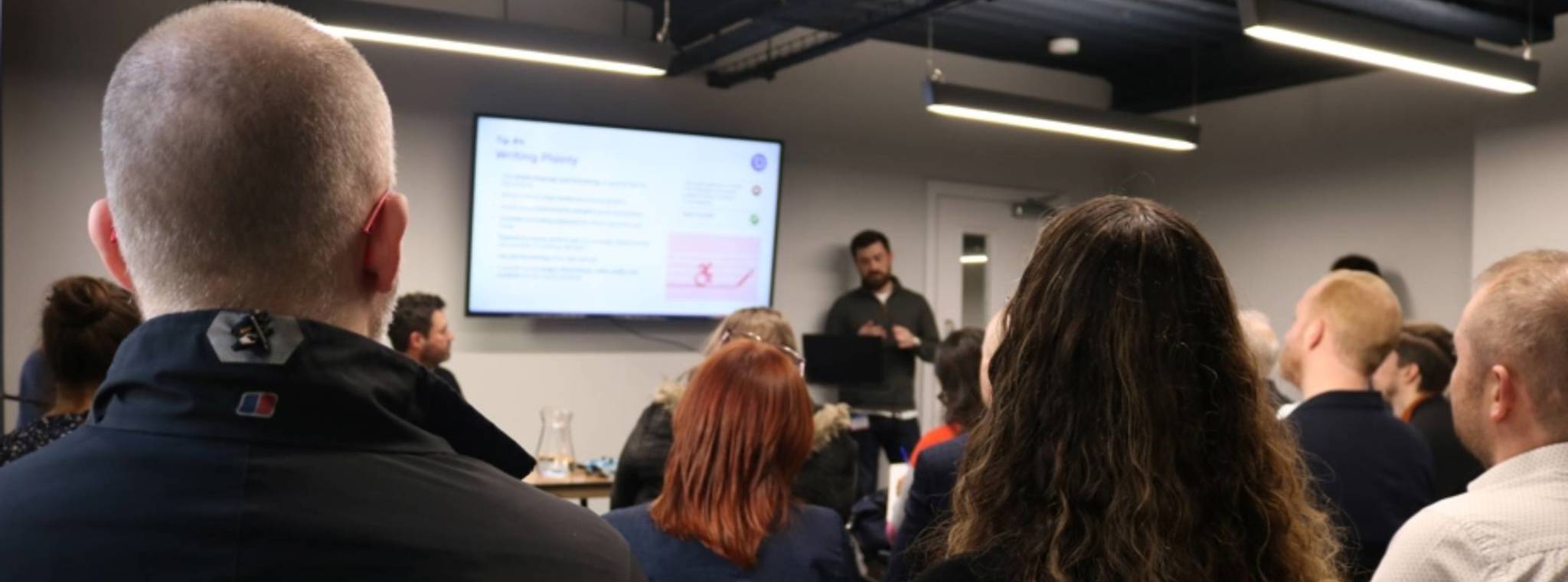 Taken from the back of the room, the back of the audiences heads with Dan Martin speaking 