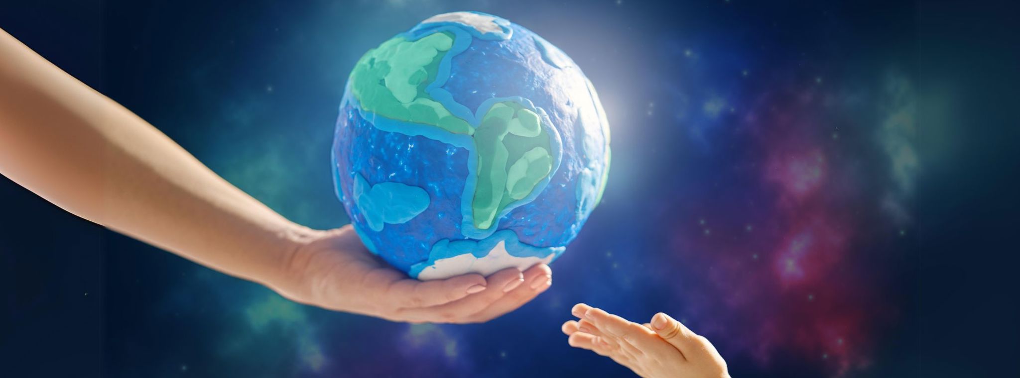 An image of an adult hand holding out a globe to a child's hand with a starry background