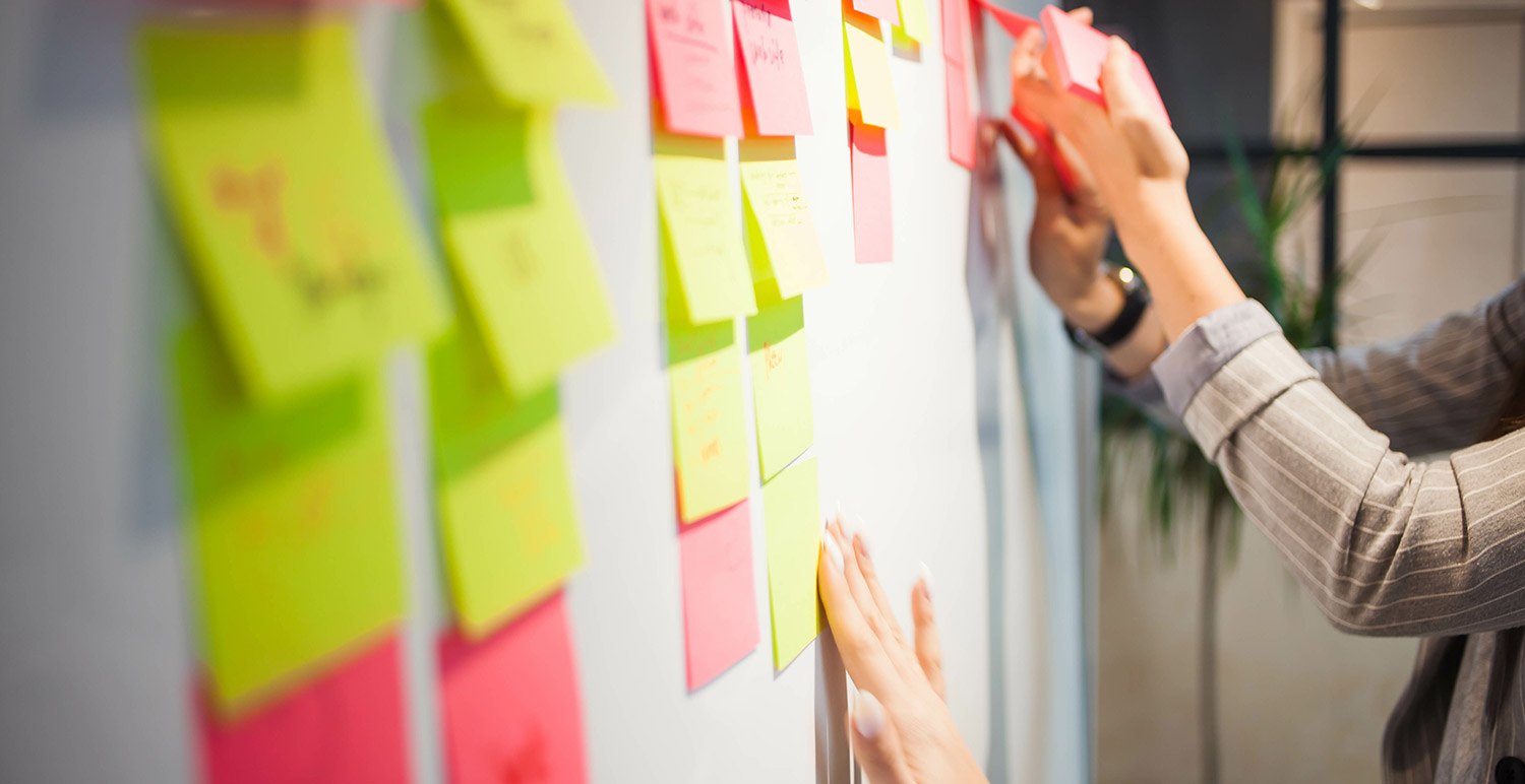 Hand placing coloured sticky notes to a whiteboard